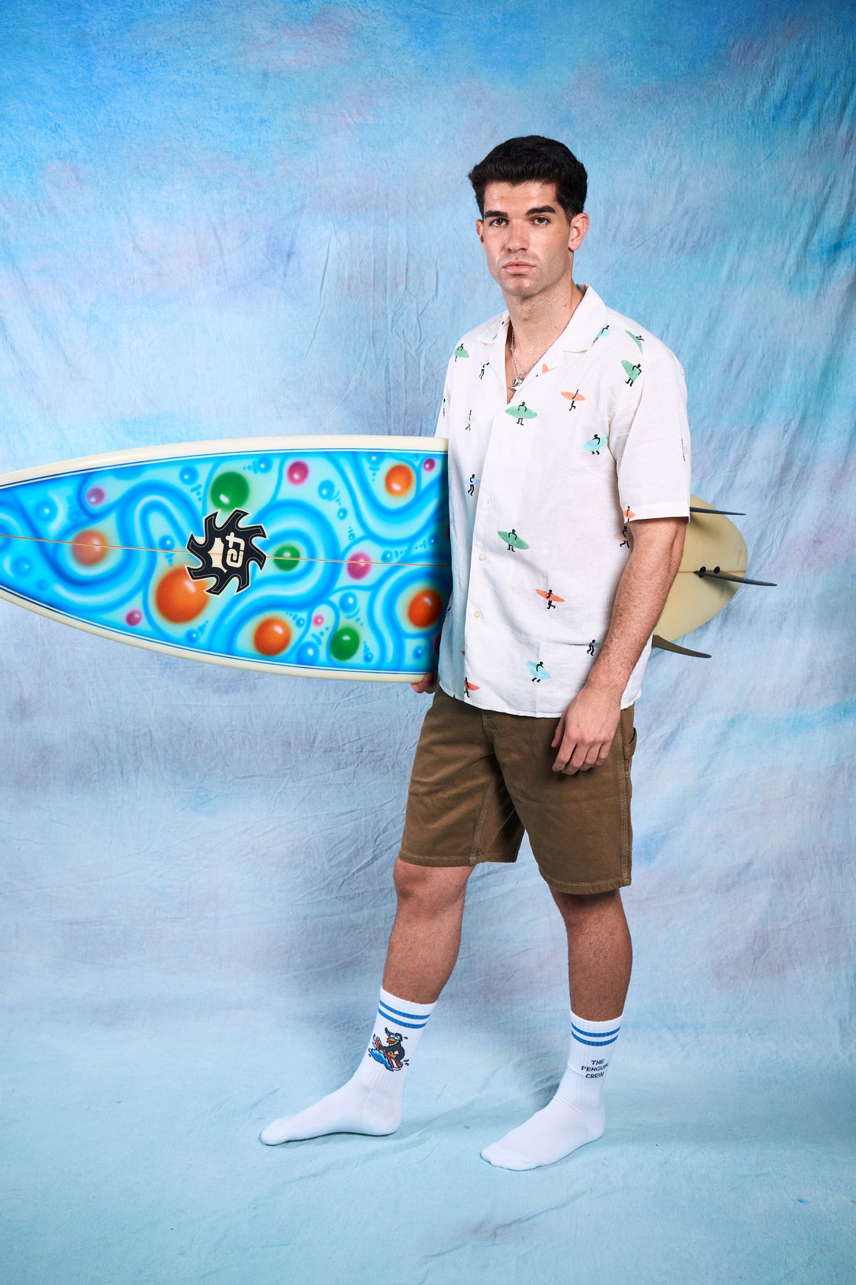 Modelo usando calcetines streetwear unisex Wave Rider con tabla de surf y camisa de estilo tropical.